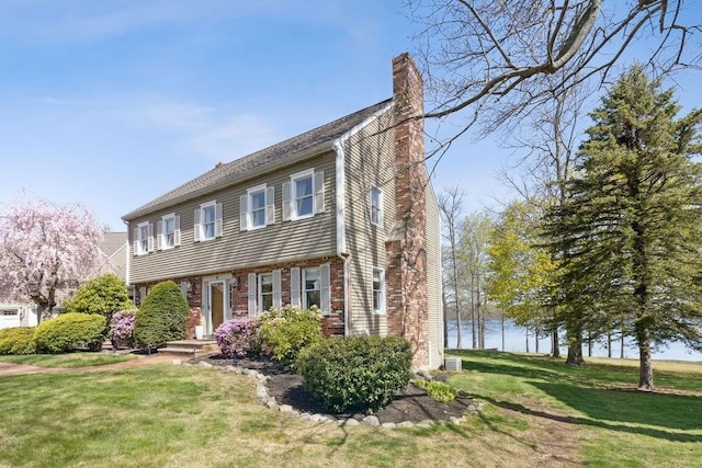 colonial inspired home with a chimney, a front lawn, and brick siding