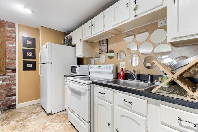 kitchen featuring white cabinets, dark countertops, a sink, white appliances, and baseboards