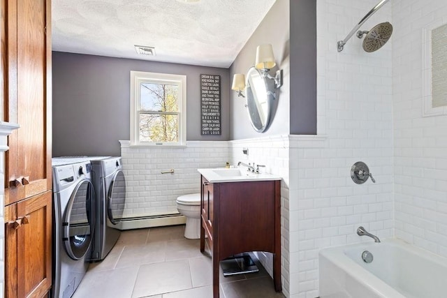 full bathroom featuring visible vents, tile patterned flooring, tile walls, washing machine and clothes dryer, and a baseboard radiator