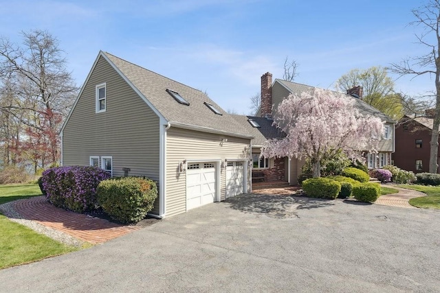 view of side of property featuring an attached garage, a chimney, a shingled roof, and aphalt driveway