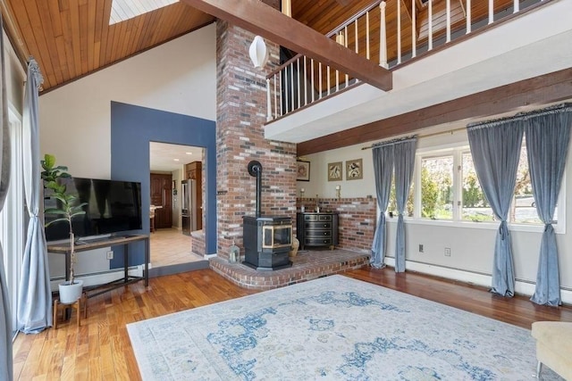 living room featuring baseboards, a wood stove, wood finished floors, and high vaulted ceiling