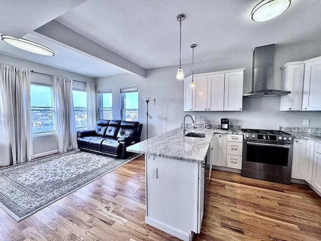 kitchen featuring stainless steel gas range oven, white cabinets, a peninsula, and wall chimney range hood