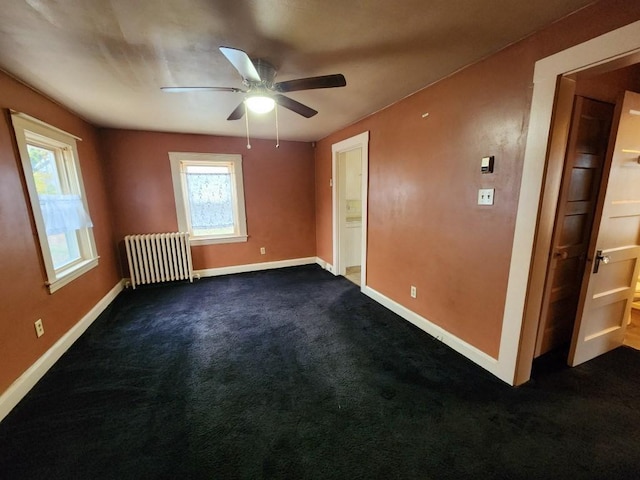 unfurnished room featuring a wealth of natural light, radiator heating unit, ceiling fan, and dark colored carpet