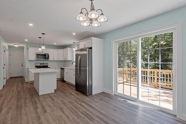 kitchen with an inviting chandelier, appliances with stainless steel finishes, decorative light fixtures, white cabinets, and a center island