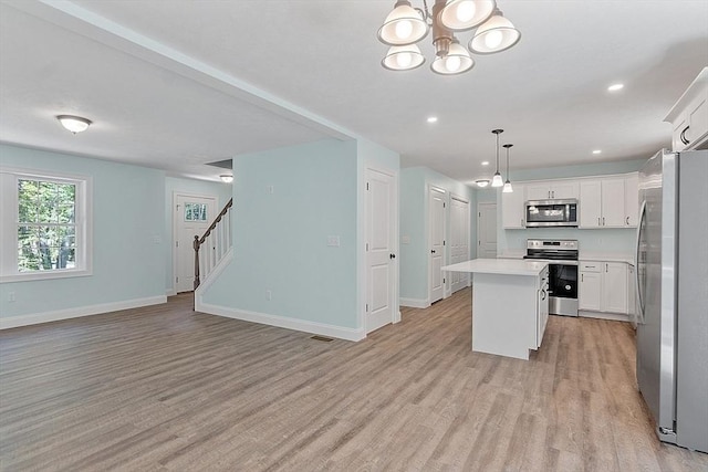 kitchen with pendant lighting, white cabinets, appliances with stainless steel finishes, a kitchen island, and light hardwood / wood-style flooring