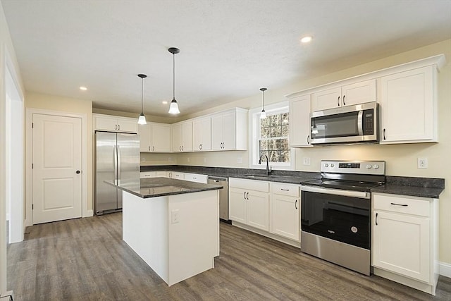 kitchen featuring appliances with stainless steel finishes, a kitchen island, dark wood-type flooring, white cabinetry, and hanging light fixtures