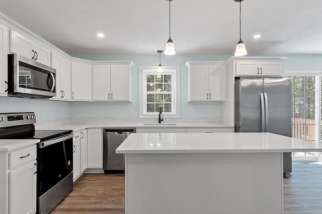 kitchen featuring decorative light fixtures, a kitchen island, sink, appliances with stainless steel finishes, and white cabinets