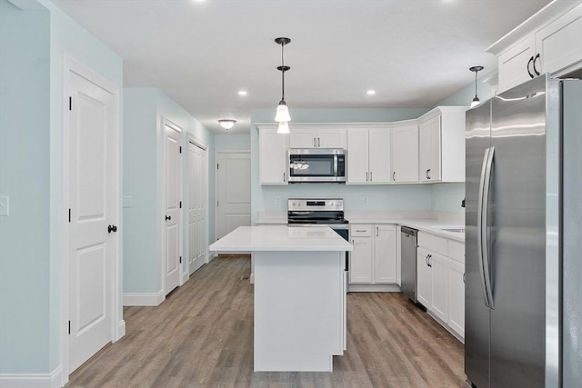 kitchen with appliances with stainless steel finishes, light wood-type flooring, hanging light fixtures, a kitchen island, and white cabinets