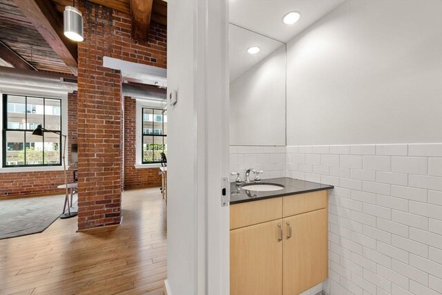 bathroom with wood finished floors, a wainscoted wall, vanity, brick wall, and tile walls