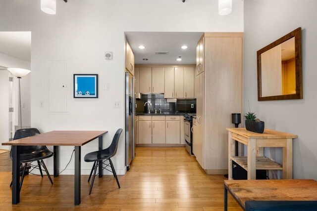 kitchen featuring light wood finished floors, stainless steel appliances, a sink, dark countertops, and recessed lighting