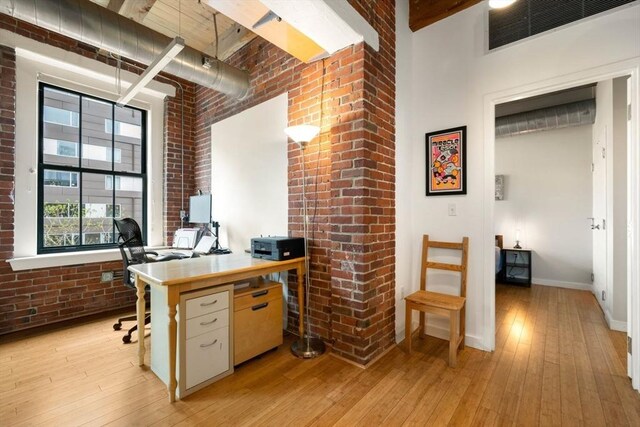 home office featuring a high ceiling, brick wall, light wood-type flooring, and baseboards