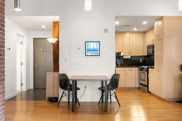 kitchen with electric range, black microwave, light brown cabinets, light wood-style flooring, and dark countertops