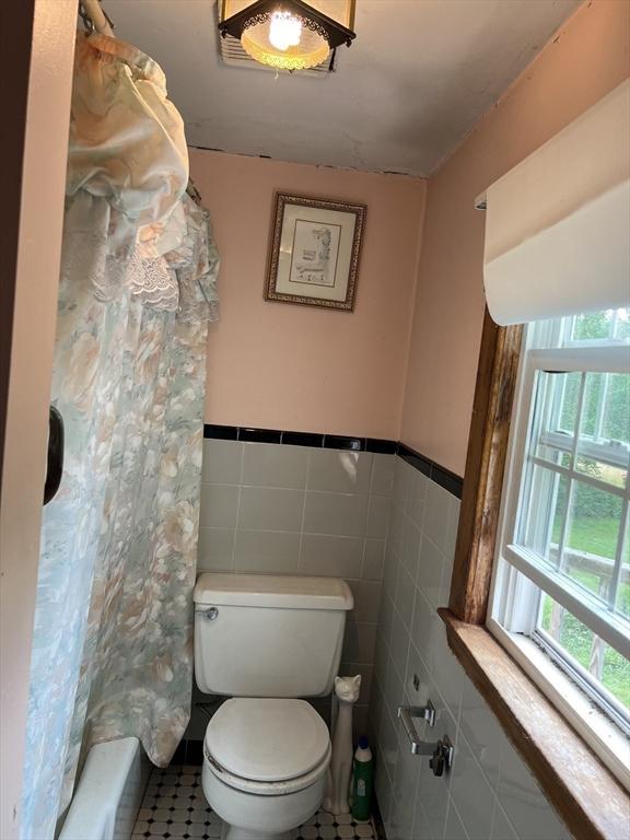 bathroom with shower / tub combo, toilet, tile patterned flooring, and tile walls