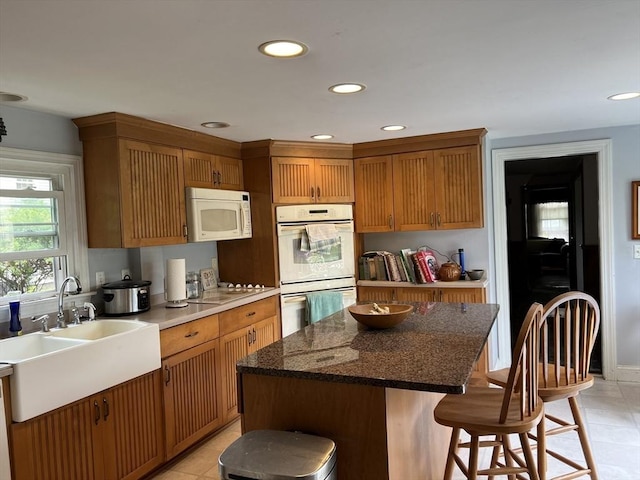 kitchen with white appliances, a breakfast bar, a center island, and sink