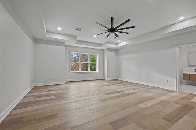 empty room featuring a tray ceiling, ceiling fan, and light hardwood / wood-style flooring