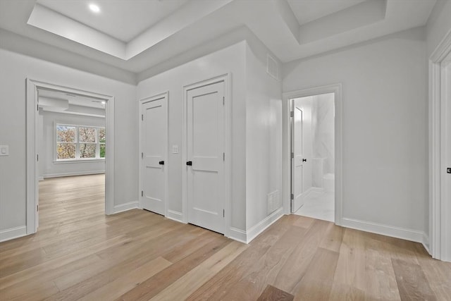 hallway with a tray ceiling and light hardwood / wood-style flooring