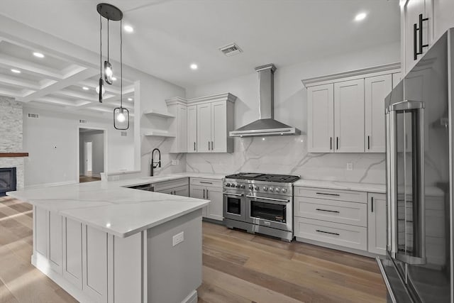 kitchen with high end appliances, coffered ceiling, wall chimney exhaust hood, beam ceiling, and kitchen peninsula