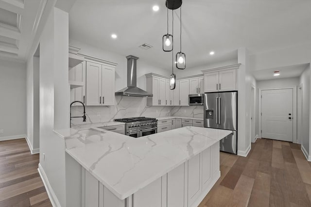 kitchen featuring light stone countertops, kitchen peninsula, wall chimney exhaust hood, stainless steel appliances, and white cabinetry