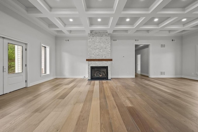 unfurnished living room with beamed ceiling, light hardwood / wood-style floors, a stone fireplace, and coffered ceiling