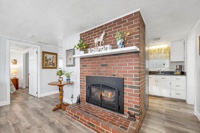 living room with a fireplace, a textured ceiling, light hardwood / wood-style floors, and sink