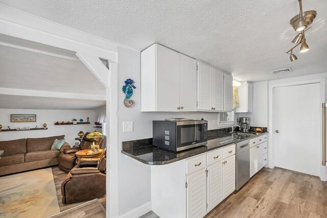 kitchen with white cabinets, a textured ceiling, stainless steel appliances, and light hardwood / wood-style flooring