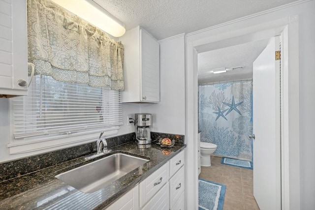 kitchen with dark stone counters, sink, a textured ceiling, light tile patterned flooring, and white cabinetry