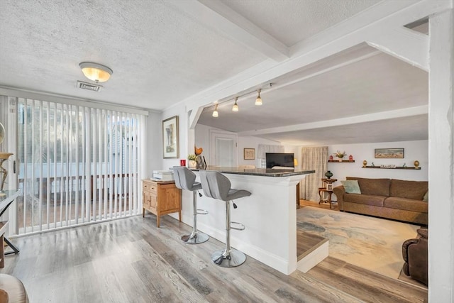 kitchen with kitchen peninsula, beamed ceiling, wood-type flooring, and a textured ceiling