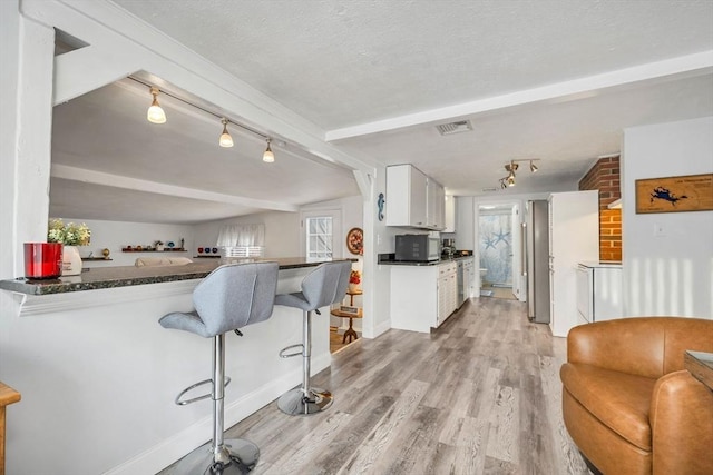 kitchen with white cabinetry, kitchen peninsula, light hardwood / wood-style floors, a textured ceiling, and a breakfast bar