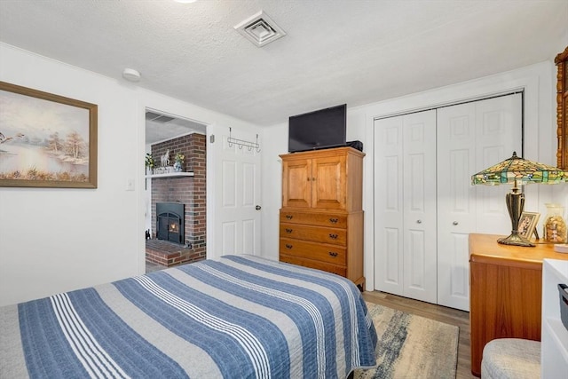 bedroom with wood-type flooring, a textured ceiling, a brick fireplace, and a closet