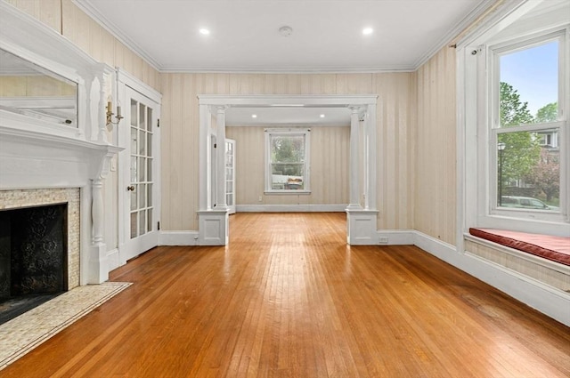unfurnished living room featuring a fireplace with flush hearth, light wood-type flooring, ornamental molding, decorative columns, and recessed lighting
