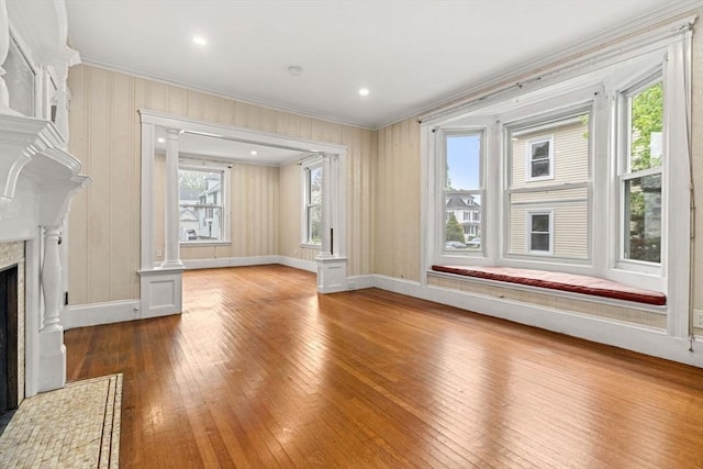 unfurnished living room with crown molding, hardwood / wood-style flooring, a fireplace, baseboards, and ornate columns