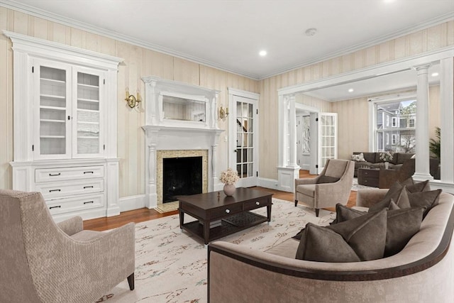 living room with ornamental molding, wood finished floors, a fireplace, decorative columns, and baseboards