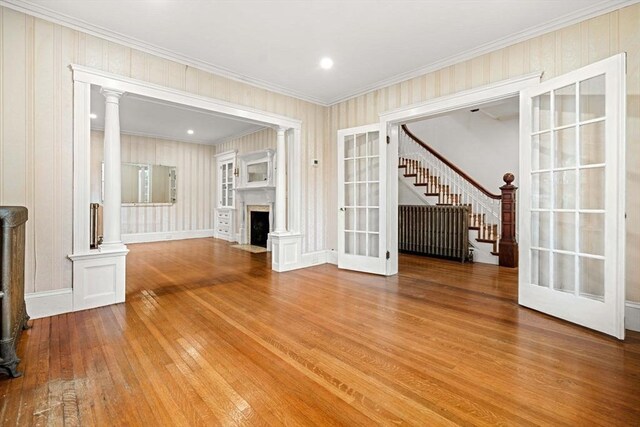 unfurnished living room featuring hardwood / wood-style flooring, stairway, decorative columns, crown molding, and a fireplace with flush hearth