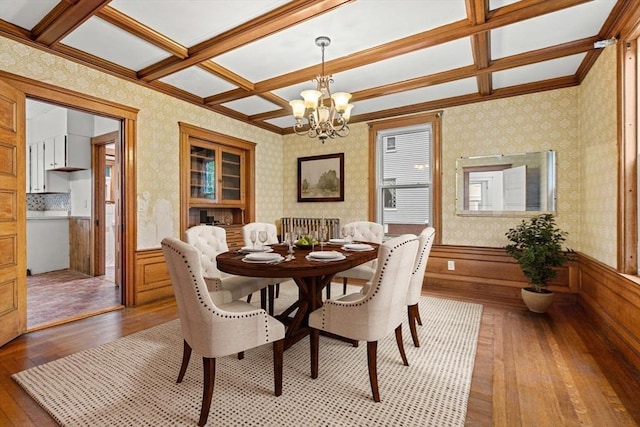 dining space featuring light wood-style flooring, a chandelier, coffered ceiling, wallpapered walls, and a wainscoted wall