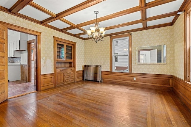 empty room with radiator heating unit, hardwood / wood-style flooring, a chandelier, a wainscoted wall, and coffered ceiling