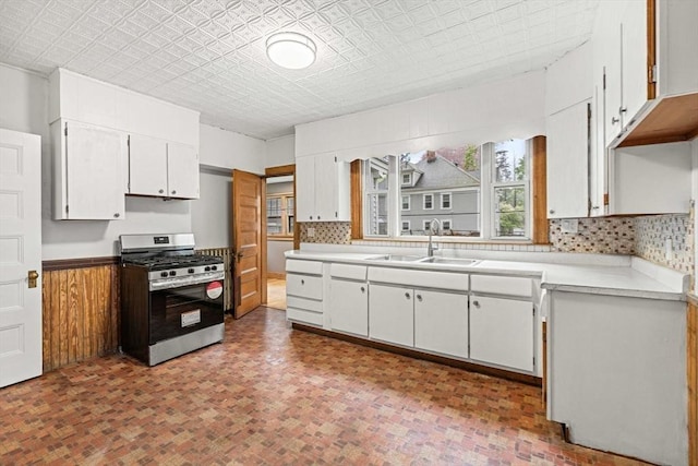 kitchen with stainless steel gas range oven, a sink, white cabinets, light countertops, and brick patterned flooring