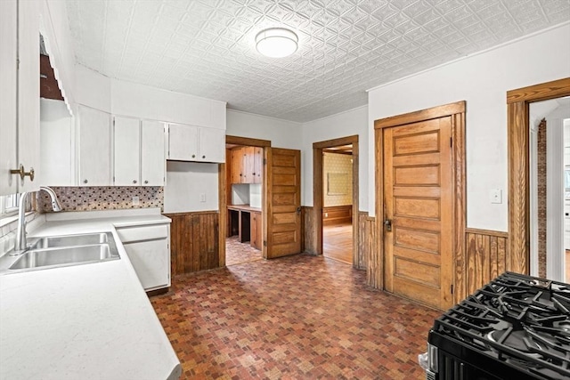 kitchen featuring a sink, a wainscoted wall, white cabinetry, light countertops, and wooden walls