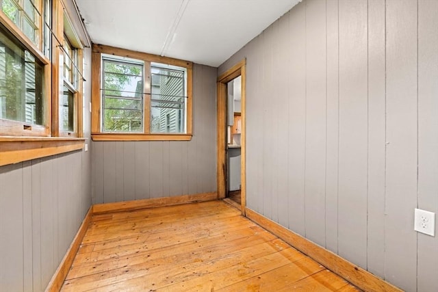 unfurnished room with light wood-style floors, baseboards, and wood walls