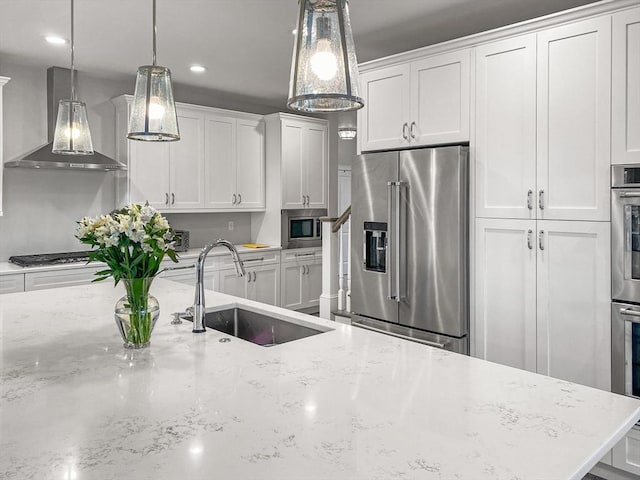 kitchen with appliances with stainless steel finishes, white cabinetry, wall chimney range hood, and a sink