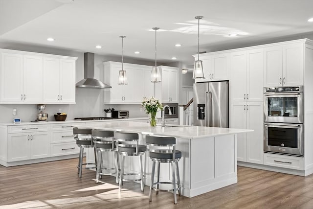 kitchen with a sink, stainless steel appliances, light wood-style floors, and wall chimney exhaust hood