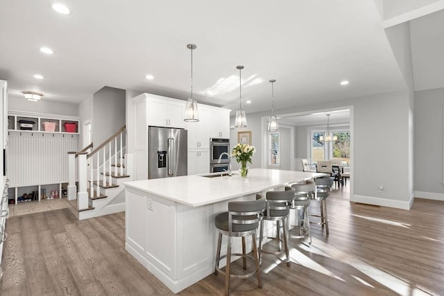 kitchen with stainless steel appliances, an island with sink, wood finished floors, and white cabinetry