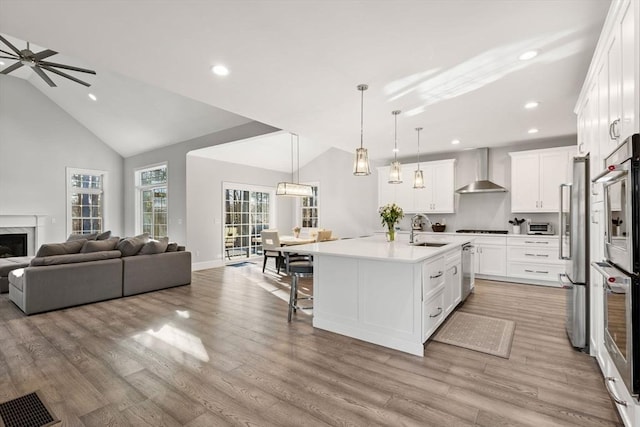 kitchen featuring a sink, vaulted ceiling, appliances with stainless steel finishes, wall chimney exhaust hood, and open floor plan