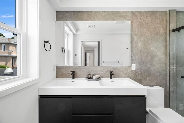 bathroom featuring toilet, a shower with shower door, tile walls, vanity, and decorative backsplash