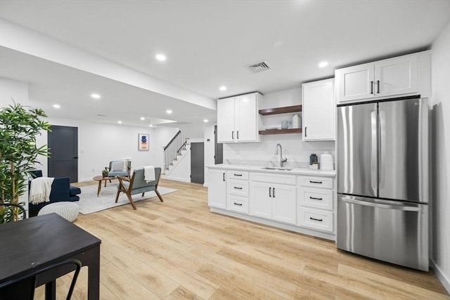 kitchen featuring white cabinets, sink, stainless steel fridge, and light hardwood / wood-style floors