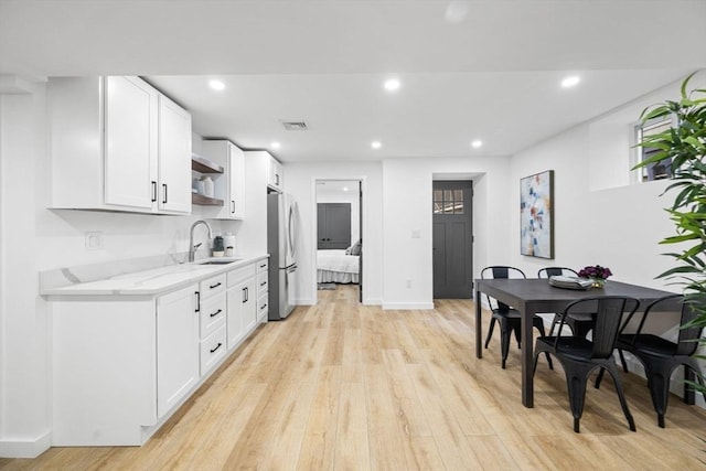 kitchen with sink, light hardwood / wood-style flooring, stainless steel refrigerator, white cabinetry, and light stone counters