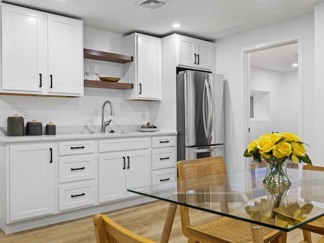 kitchen with white cabinets, sink, stainless steel fridge, and light wood-type flooring