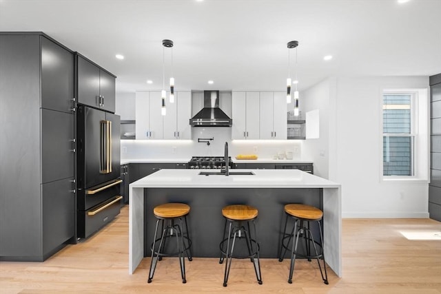 kitchen featuring white cabinetry, wall chimney range hood, high end refrigerator, and hanging light fixtures