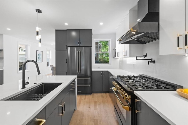 kitchen featuring sink, premium appliances, pendant lighting, wall chimney range hood, and white cabinets