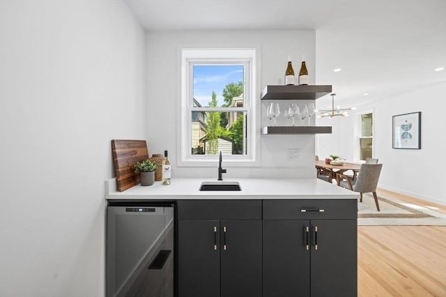 bar featuring dishwashing machine, sink, and light hardwood / wood-style flooring