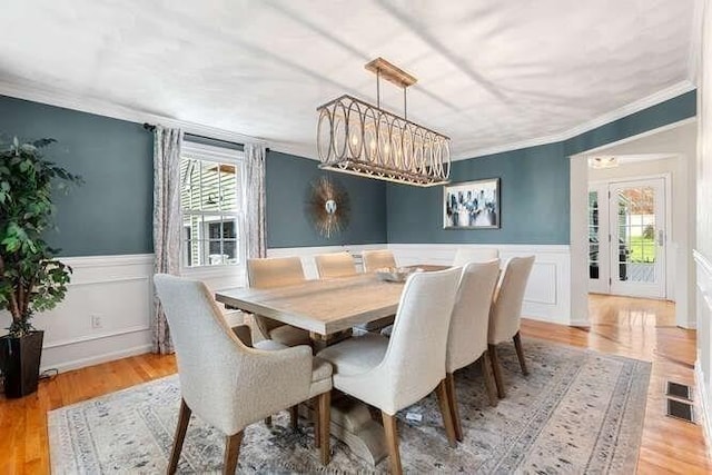 dining room with crown molding, a wainscoted wall, light wood-type flooring, and a decorative wall